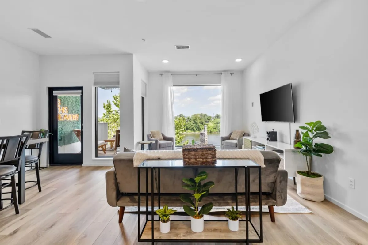 A welcoming living area featuring a cozy seating arrangement, decorative plants, a TV mounted on the wall, and a large window with a view to the outside. The space exudes comfort, perfect for unwinding with family after city adventures.