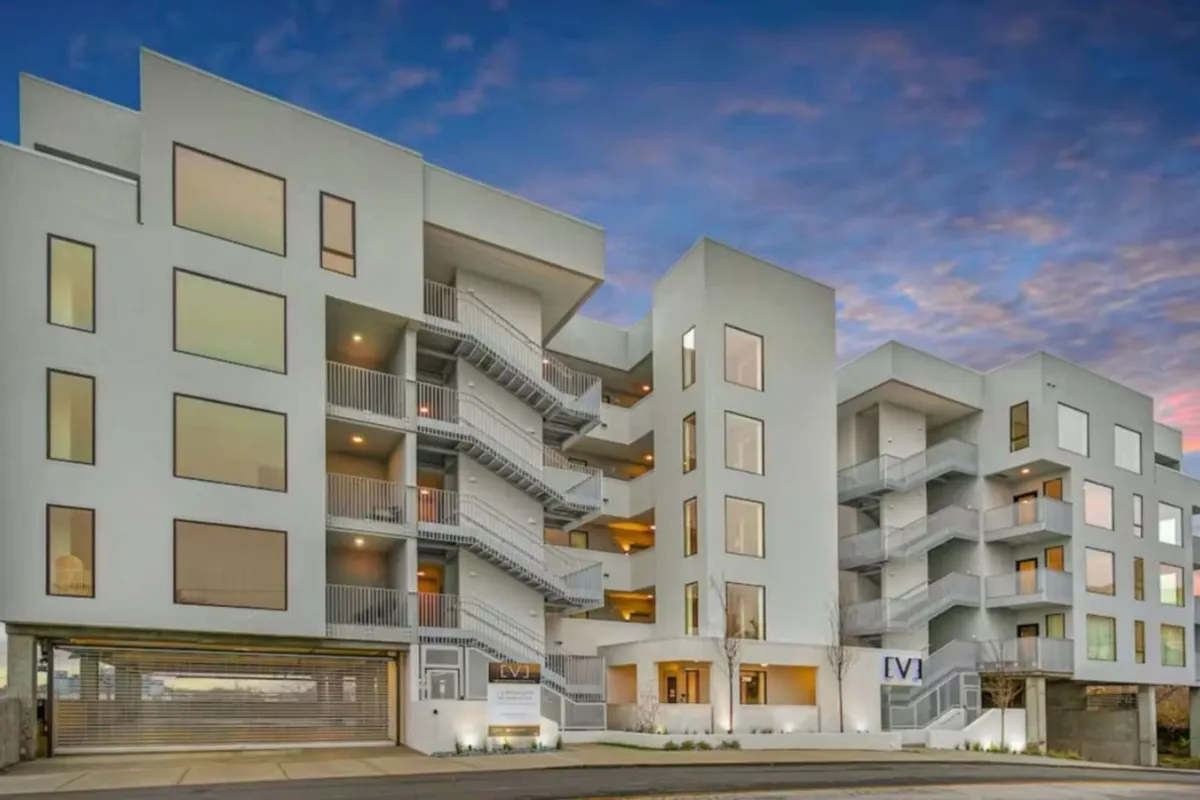 An exterior shot highlighting the property's modern architecture, balconies, and landscaped surroundings. The scene projects an urban vibe with vibrant community energy, capturing the building's city-edge appeal.