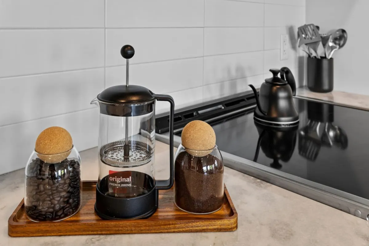 A cozy breakfast nook set for a morning coffee experience, displaying a French press, coffee bean jar, ground coffee jar, and a kettle. Warm lighting and a sense of togetherness create an inviting atmosphere for enjoying coffee and conversation.