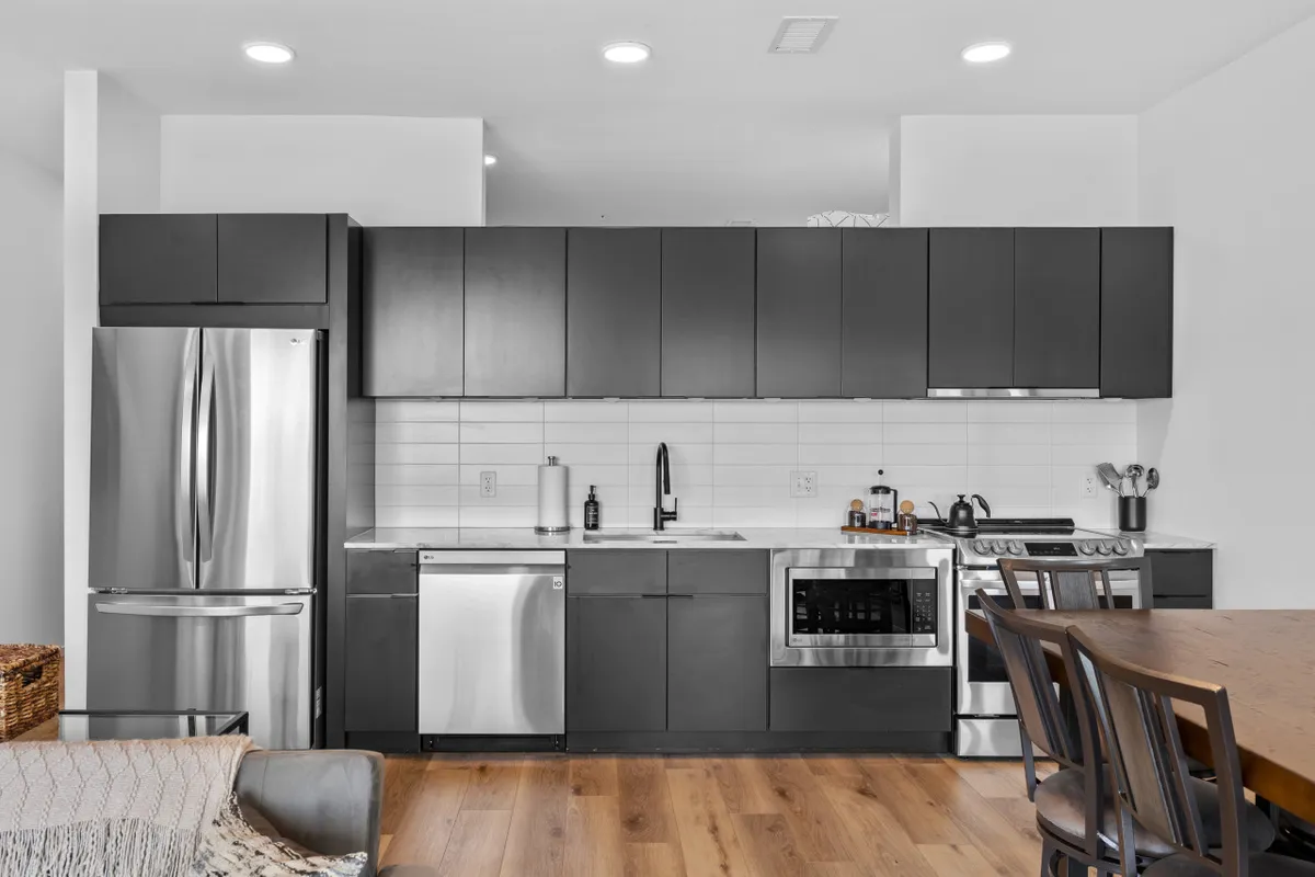A modern kitchen featuring stainless steel appliances, dark cabinetry, and a sturdy wooden dining table. The space is uncluttered and primed for culinary activity, with ample room for cooking and entertaining.