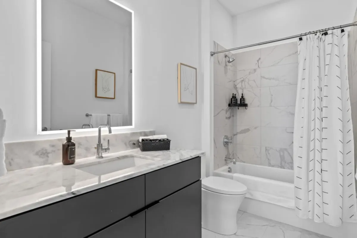 A modern bathroom with a marble vanity, backlit mirror, spacious shower area, and framed artwork. The space is bright, clean, and reminiscent of a spa, perfect for self-care routines and refreshing starts.